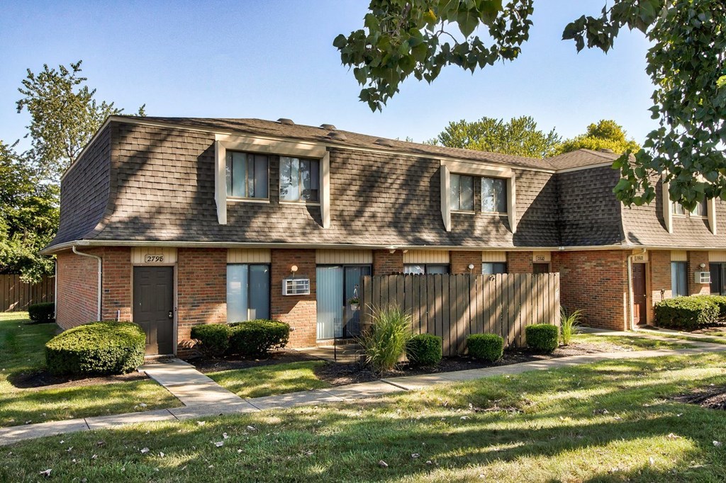 A house with a brown roof and a grey door is surrounded by green bushes.