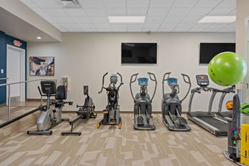 A gym with a variety of exercise equipment including treadmills, stationary bikes, and elliptical machines.
