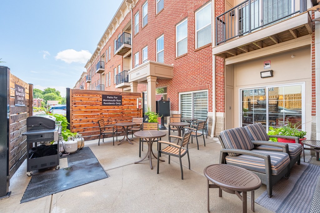A patio with a grill and chairs is surrounded by a brick building.
