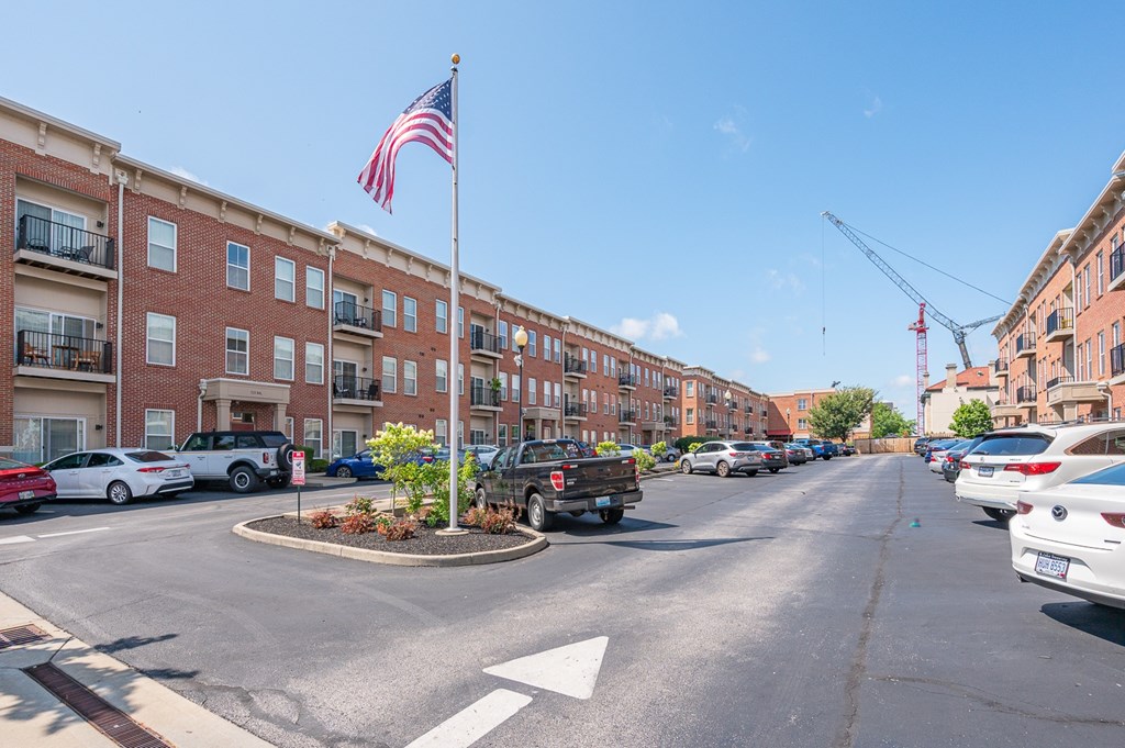 A street view with a flag on a pole and cars parked on the side.