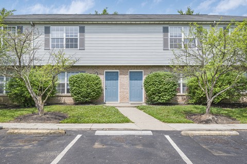 A grey building with a blue door and two trees in front.