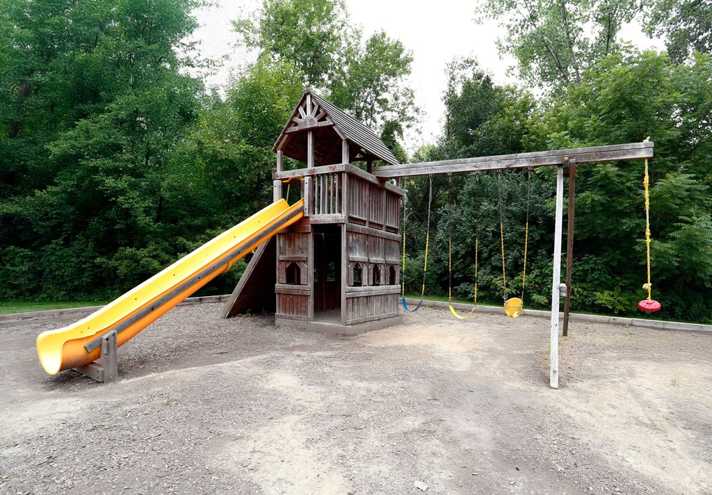 A playground with a yellow slide and a wooden swing set.