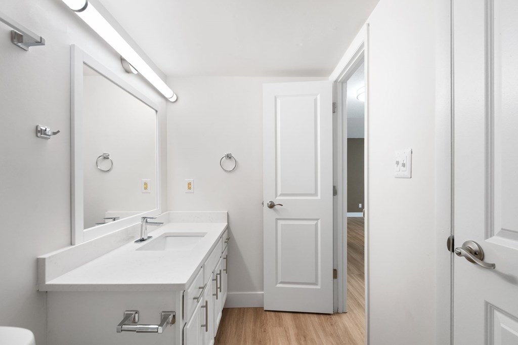 A white bathroom with a sink, mirror, and toilet.