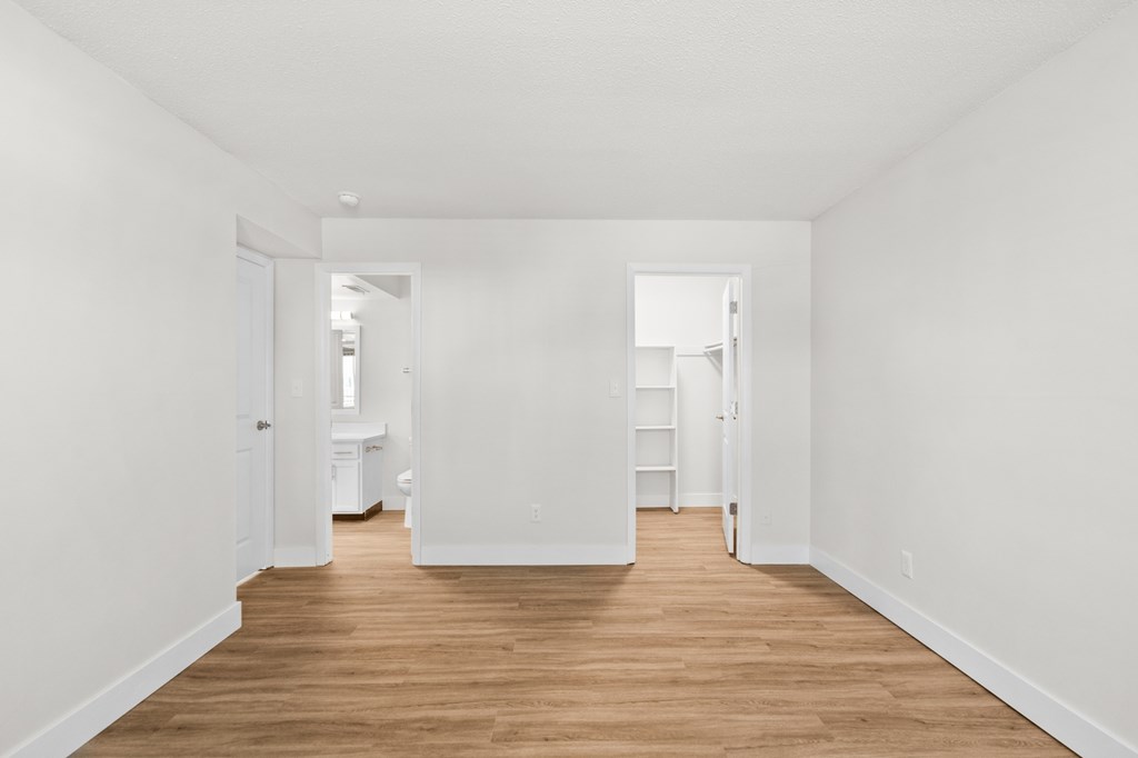 A long, narrow, white hallway with wood floors and white walls.