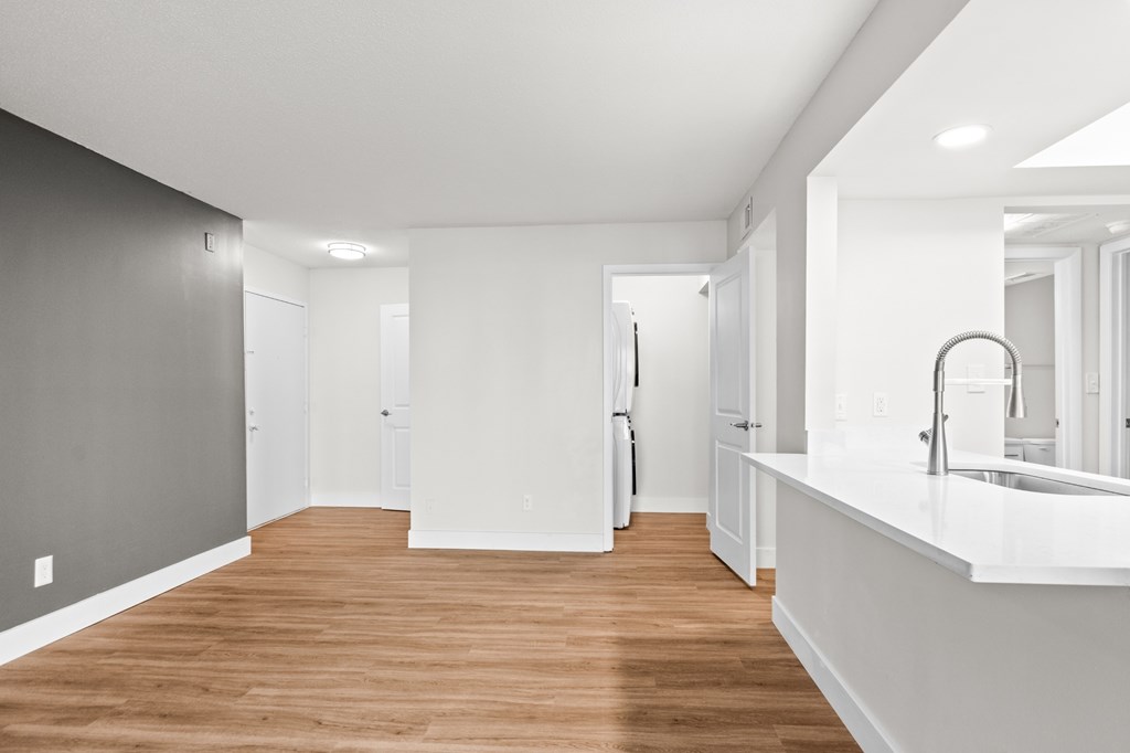 A long, narrow, white hallway with wood floors and white walls.
