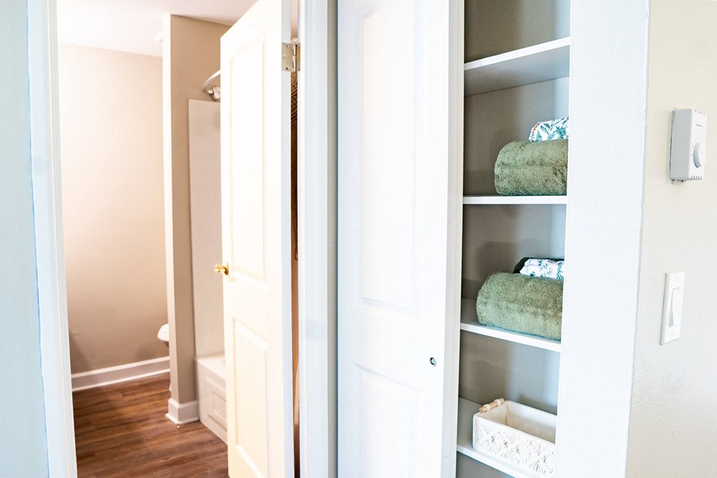 a closet with a white door and white shelves with blue and green towels
