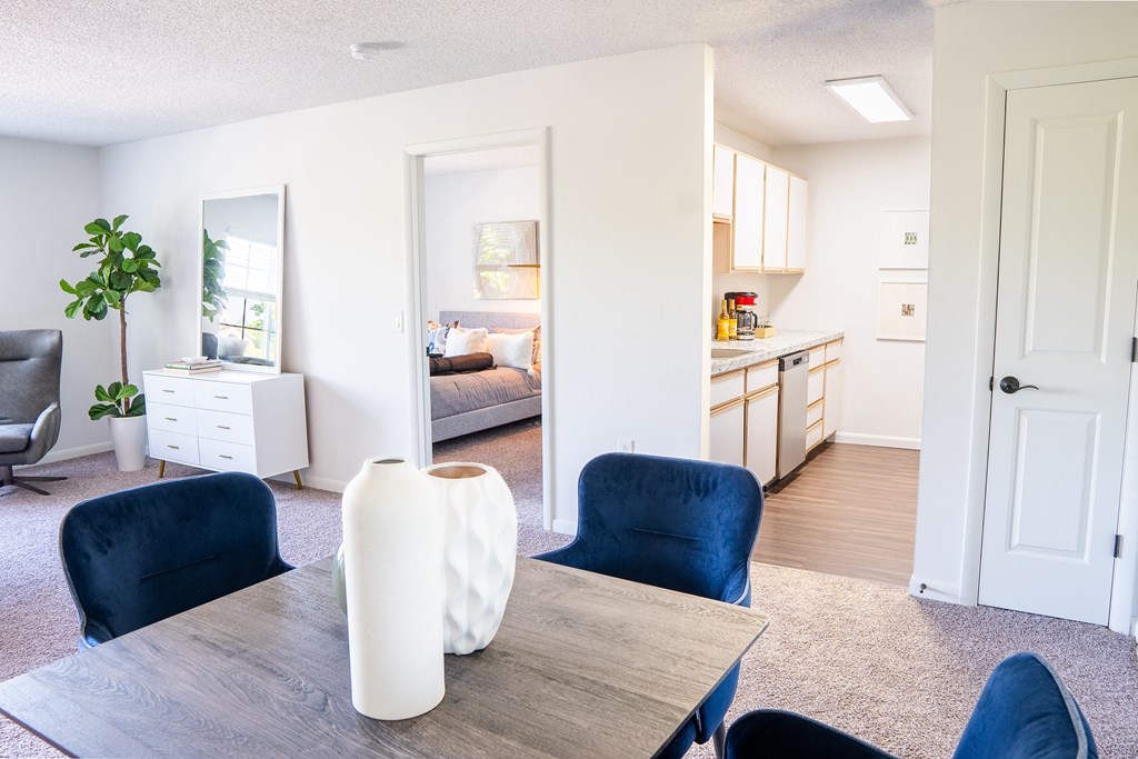 a living room with a dining room table and chairs and a kitchen in the background