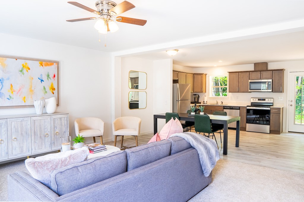 a living room with a blue couch and chairs and a kitchen with wooden cabinets and stainless steel