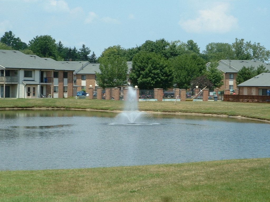 a fountain in the middle of a pond in front of an apartment building