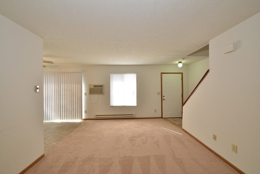 A room with a carpeted floor and a staircase on the right side.