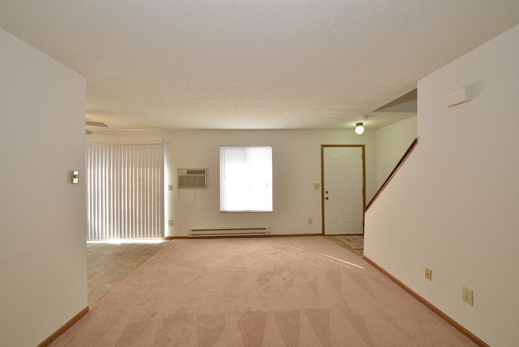 A room with a carpeted floor and a staircase on the right side.
