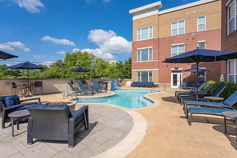 A pool surrounded by chairs and umbrellas with a building in the background.