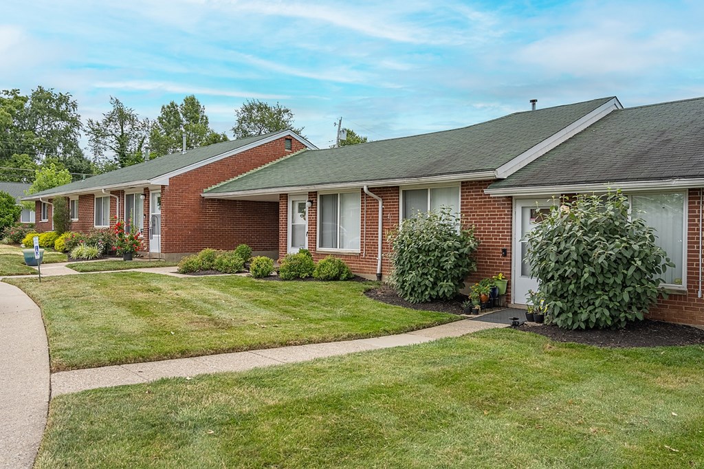 A row of houses with green lawns and trees in the background.