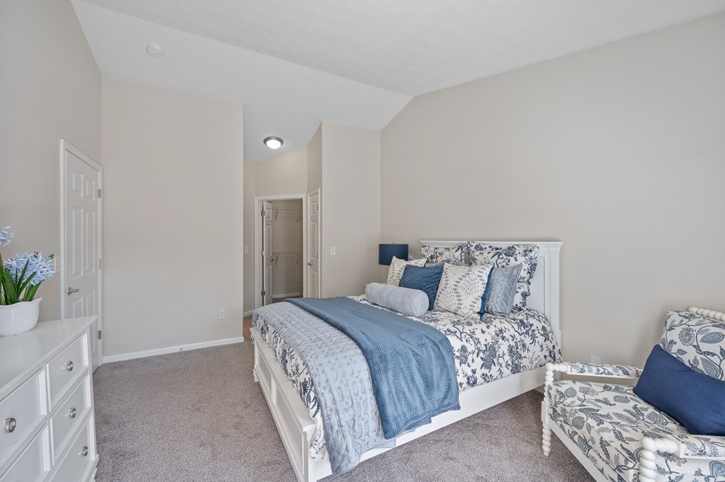 A bedroom with a bed, chair, and nightstand.
