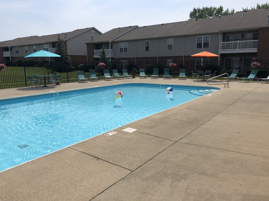 A swimming pool with a blue umbrella and chairs around it.