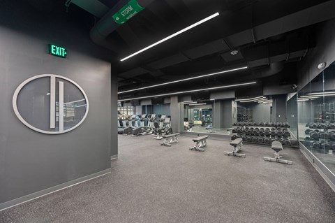 A gym with a green exit sign and a clock on the wall at Sky Central Apartments, Cincinnati