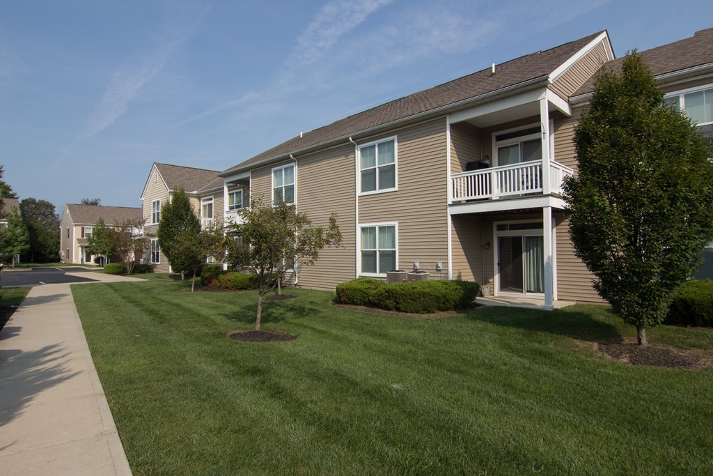 a grassy area with trees and bushes in front of a building  at Grove City Summit, Grove City, OH