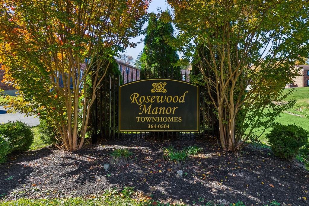 A sign for Rosewood Manor Townhomes is surrounded by trees.