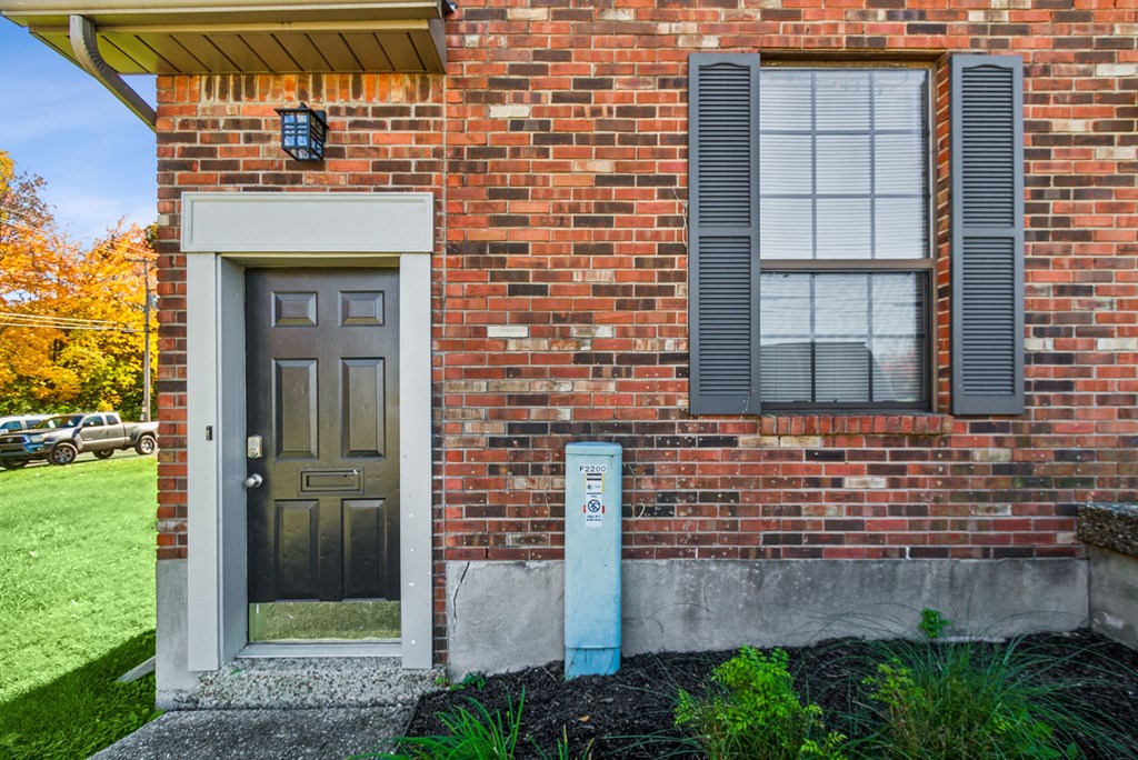 A brick house with a grey door and a window with black shutters.