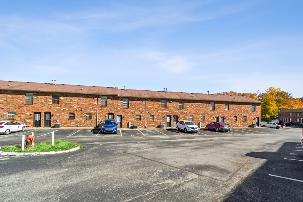 A parking lot in front of a brick building with cars parked.