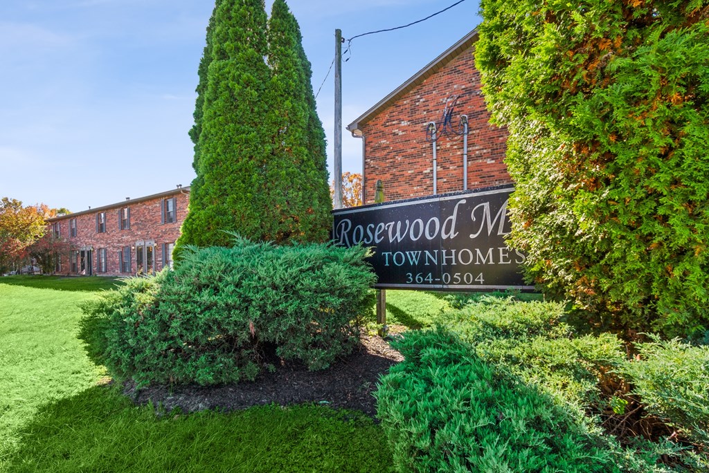 A sign for Rosewood Manor Townhomes stands in front of a brick building.