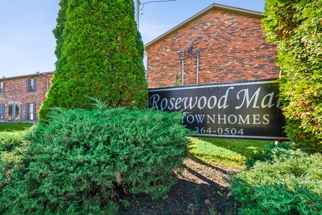 A sign for Rosewood Manor Townhomes is in front of a brick building.
