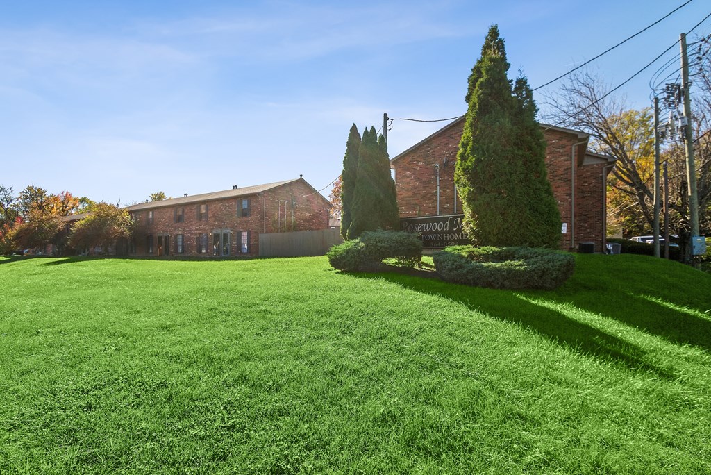 A green lawn in front of a brick building with trees.