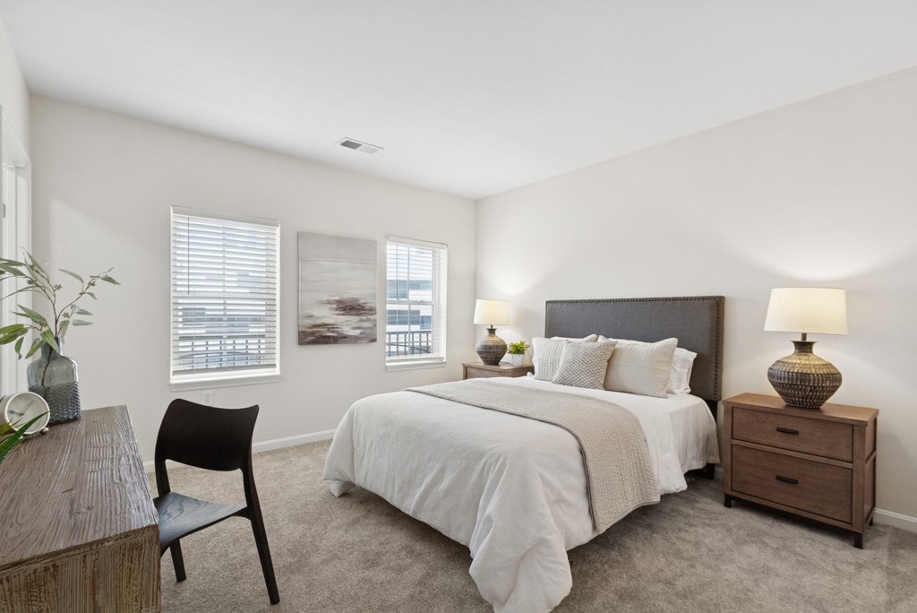 A bedroom with a bed, nightstand, chair, and a plant.
