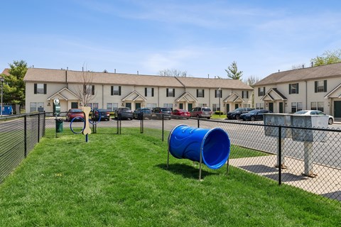 A blue barrel is in the grass in front of a chain link fence.