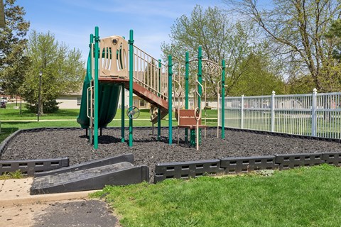 A playground with a green slide and a brown and green play structure.