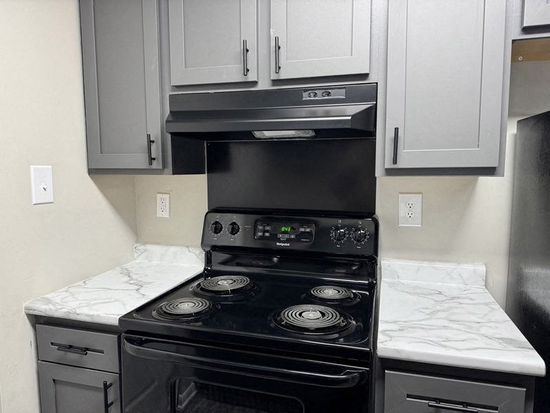 A modern kitchen with a black stove top oven and white cabinets at Quail Run Apartments, Indiana