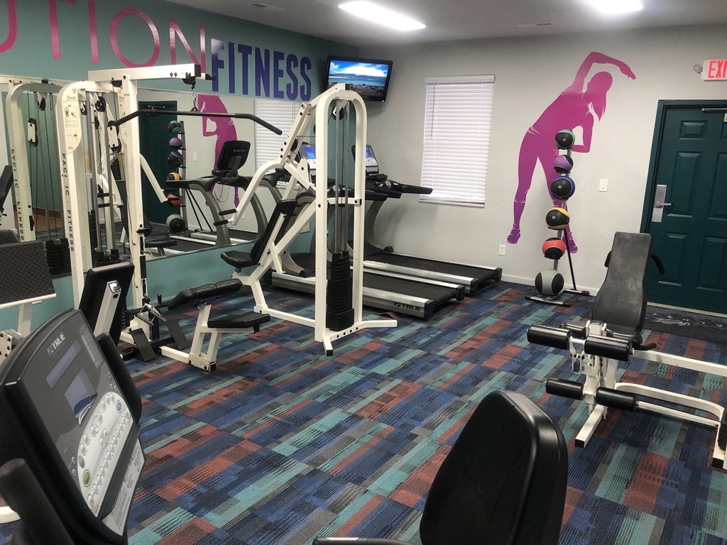 A gym with a variety of equipment including treadmills, weights, and exercise machines.