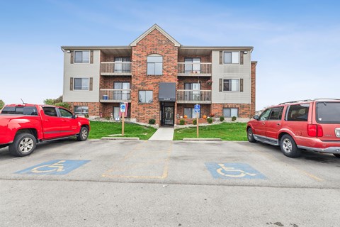 A red truck is parked in a handicapped spot in front of a brick apartment building.