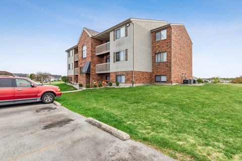A red car is parked in a parking lot in front of a brick apartment building.