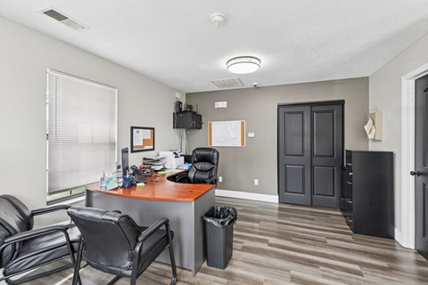 A room with a desk, chairs, and a trash can.