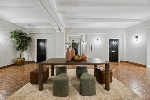 A room with a table surrounded by green poufs and a plant in a pot.
