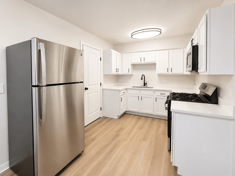 A kitchen with a refrigerator, cabinets, and a counter.