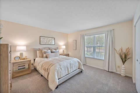 A bedroom with a large bed and a window with curtains.