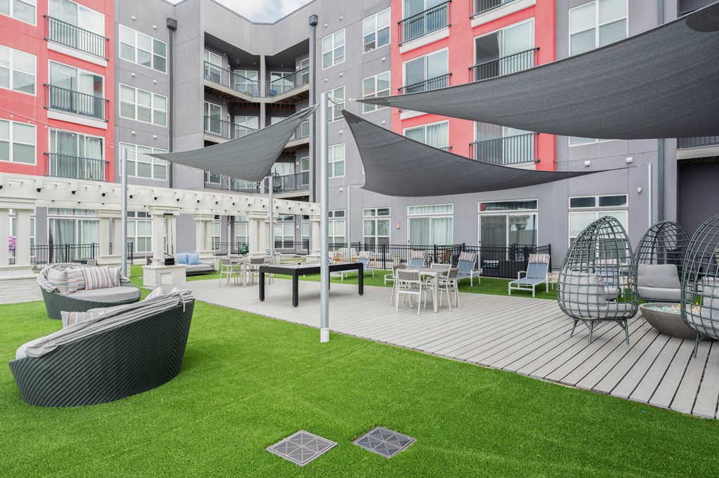 an outdoor lounge area with chairs and umbrellas in front of an apartment building