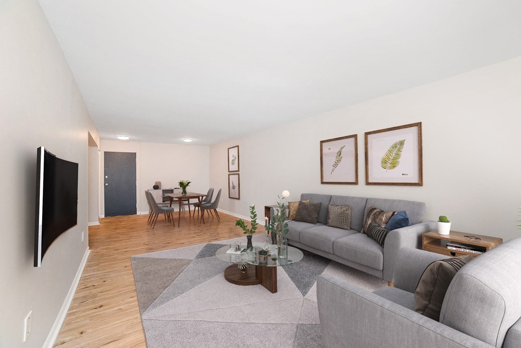 A living room with a grey couch, a coffee table, a dining table, and a television at The Alpine Apartments, Kettering, OH