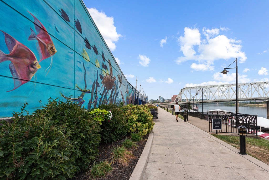 a large mural on a wall next to a river with a bridge at Monmouth Row Apartments, Newport, KY