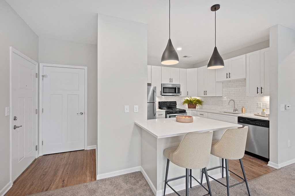 a kitchen with white cabinets and a white island with two stools at Monmouth Row Apartments, Newport, KY, 41071