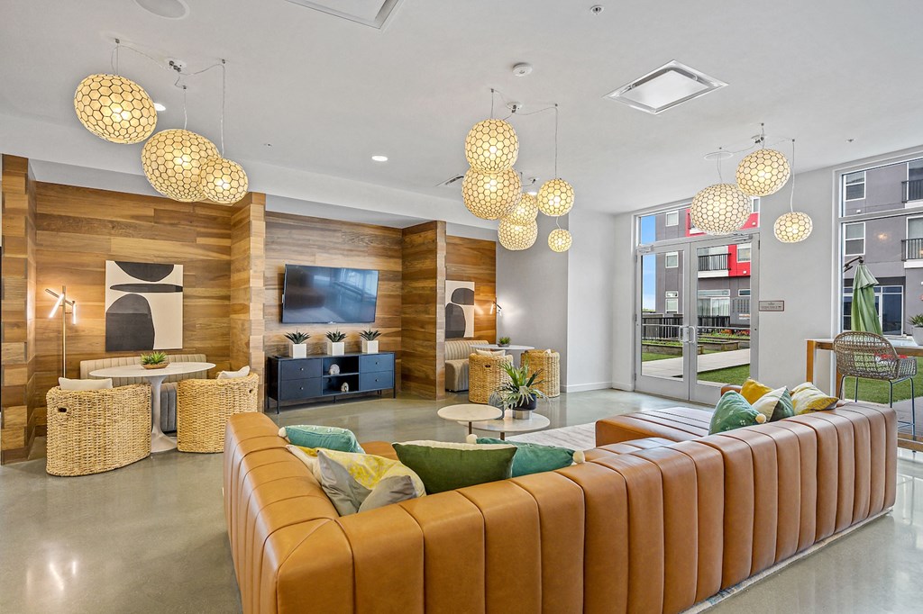 Apartments in Liberty Township, OH, with In-Unit Washer and Dryer - Liberty Center - Community Lounge with Leather Sectional Couch, Booth-Style Seating, Media Cabinet, Wall-Mounted TV, Glass Doors, and Floor-to-Ceiling Windows.