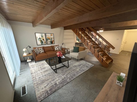 A living room with a brown couch and a wooden staircase.