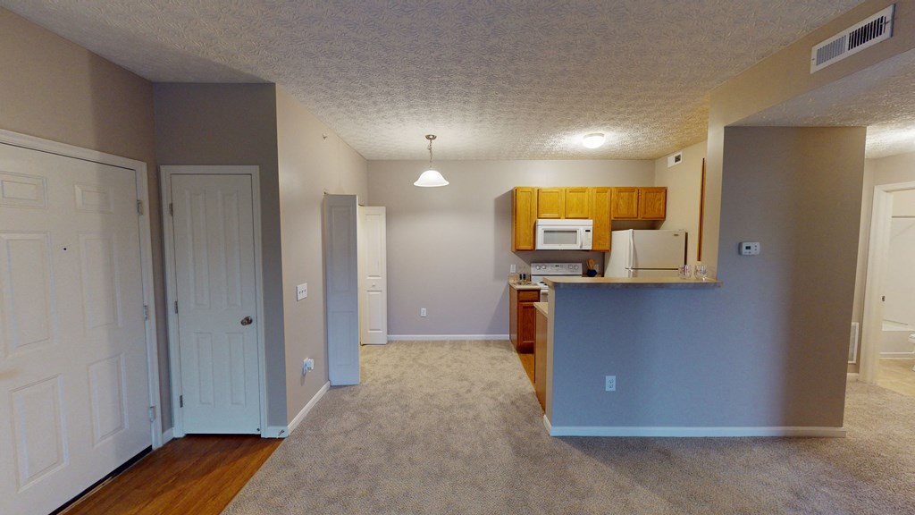 an empty living room with a kitchen and a door to a hallway at Prescott Place, Columbus, 43235