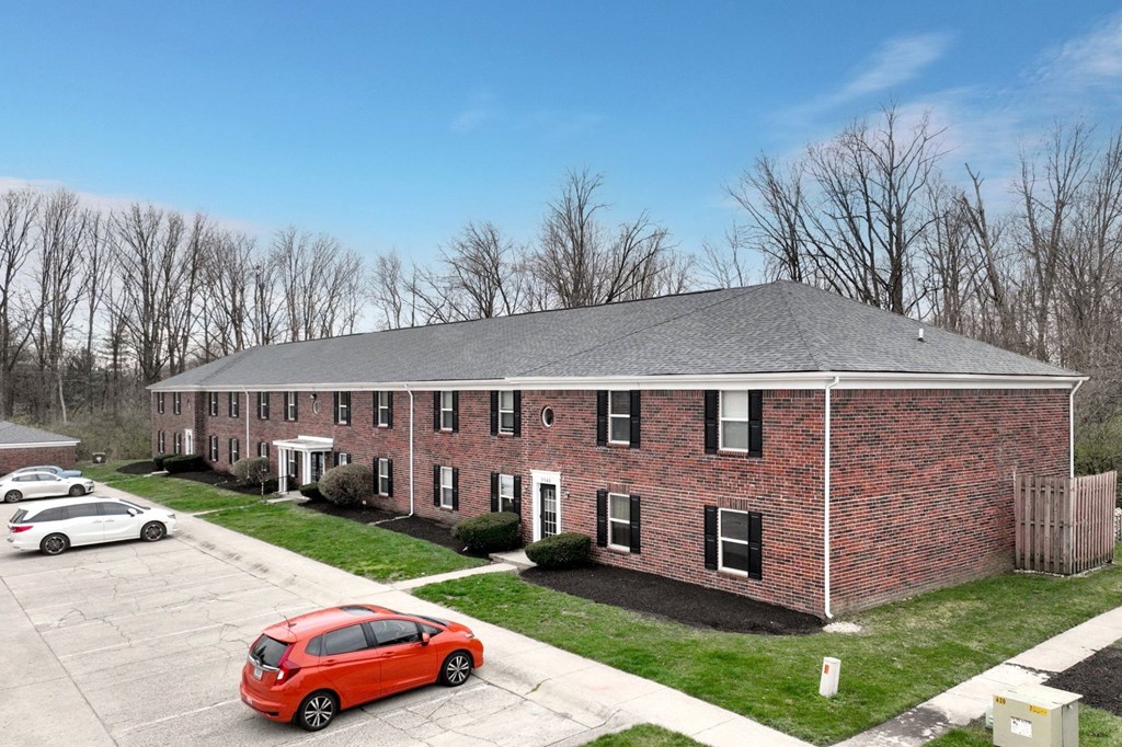 A red car is parked in a parking lot in front of a brick building.