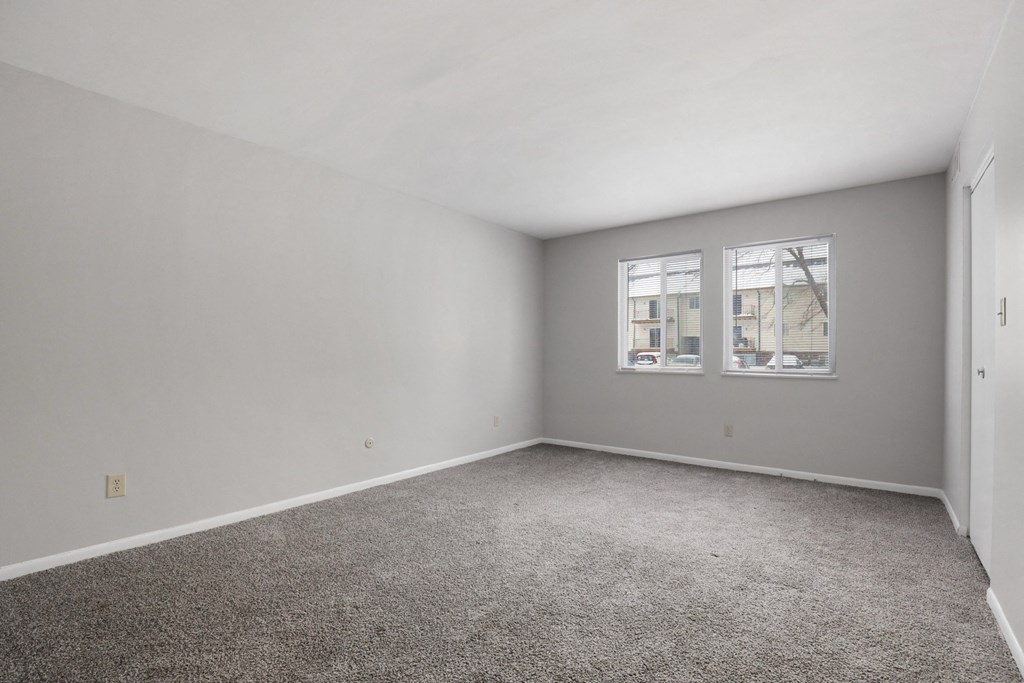A room with grey carpet and two windows.