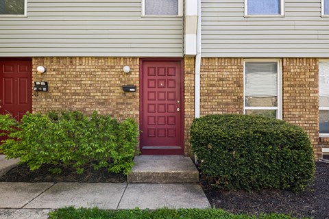 A red door is on the left side of a brick building. at Sharon Green Townhomes, Columbus, Ohio