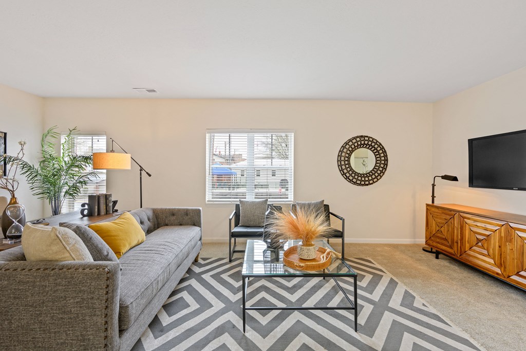 a living room with a gray couch and a glass coffee table on a chevron rug