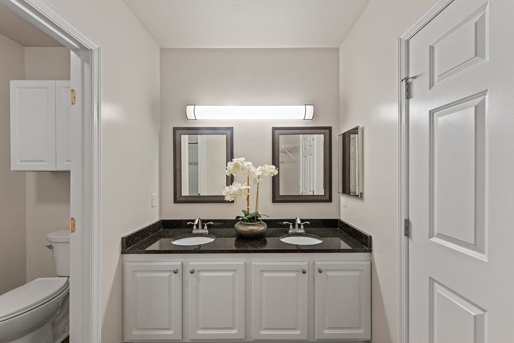 a bathroom with white cabinets and a black counter top with two sinks